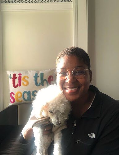 Dark-skinned woman with glasses poses with a small white dog